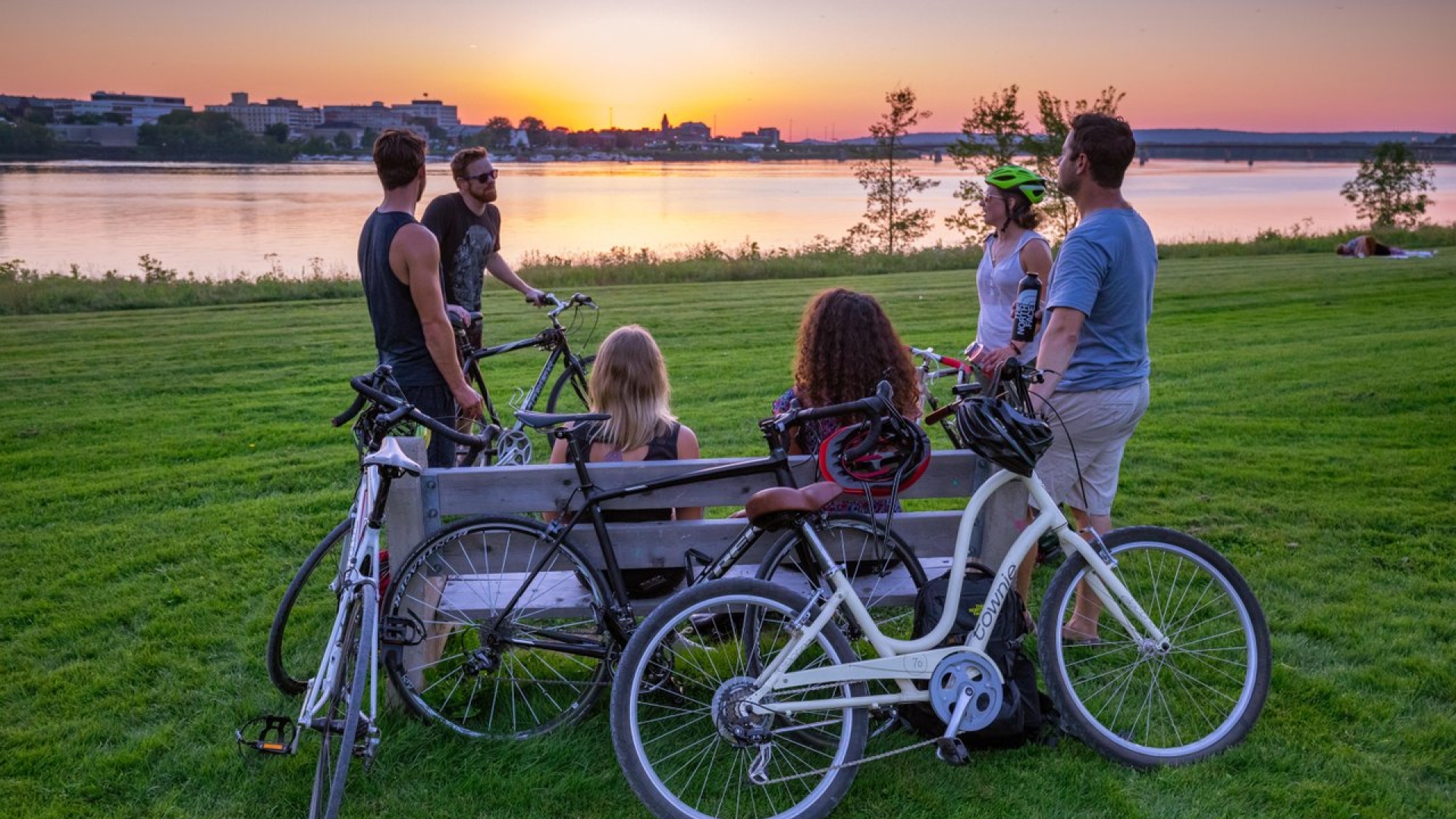 Group of people sitting on a park bench looking the sunset over the river