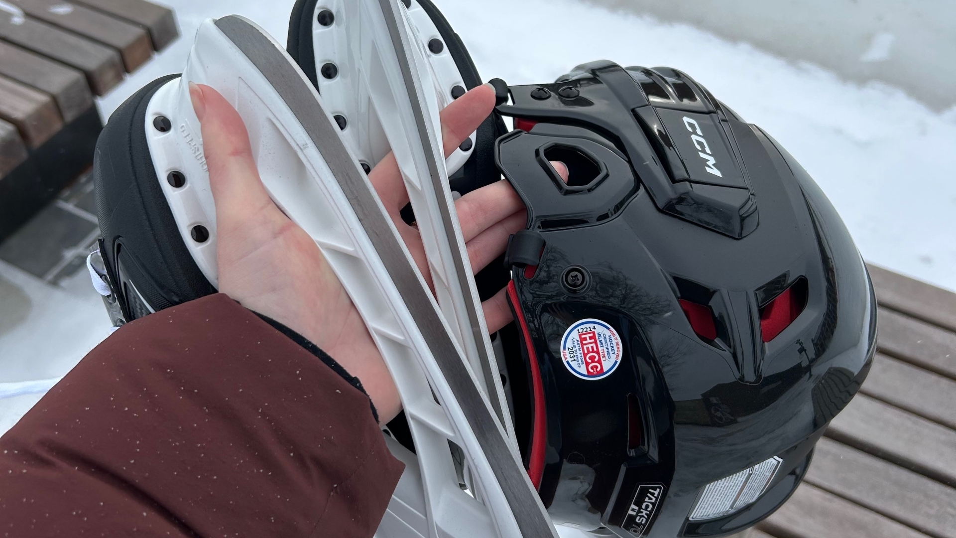Hand holding skates and helmet above ice