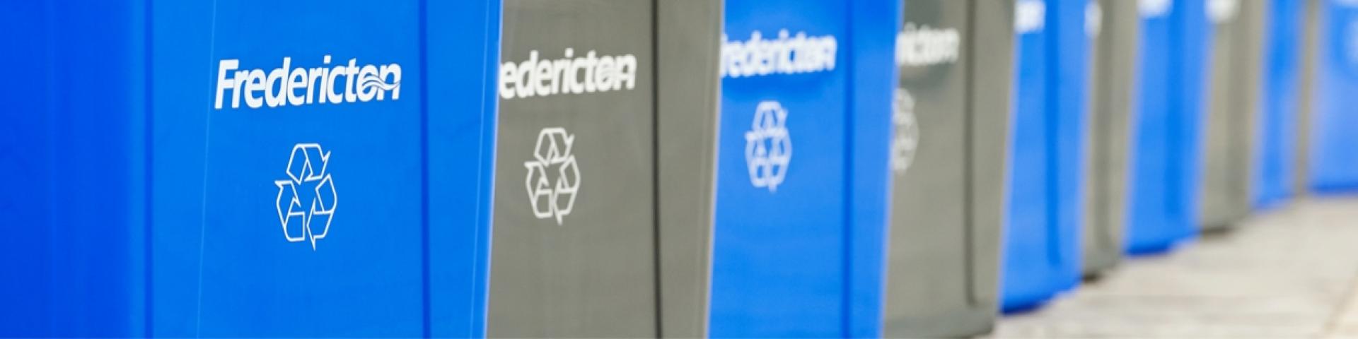 Row of blue and gray Fredericton recycling bins.
