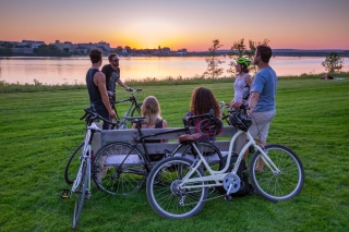 Group of people sitting on a park bench looking the sunset over the river