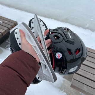 Hand holding skates and helmet above ice