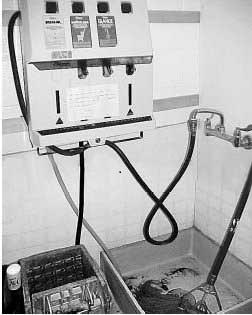 A utility tap with a shallow tub below in a corner. Tubes run from the tap to a cleaning solution dispenser.