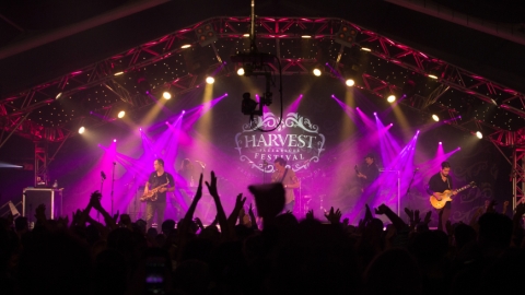 Band on stage with purple light shining on them with fans in front of the stage